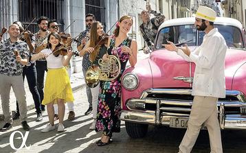 Sarah Willis steht mit jungen Musikerinnen und Musikern vor einem alten Auto